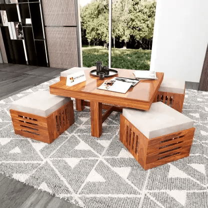 This is a square-shaped solid wood center table with a natural honey finish accompanied by 4 cream-coloured cushion stools.